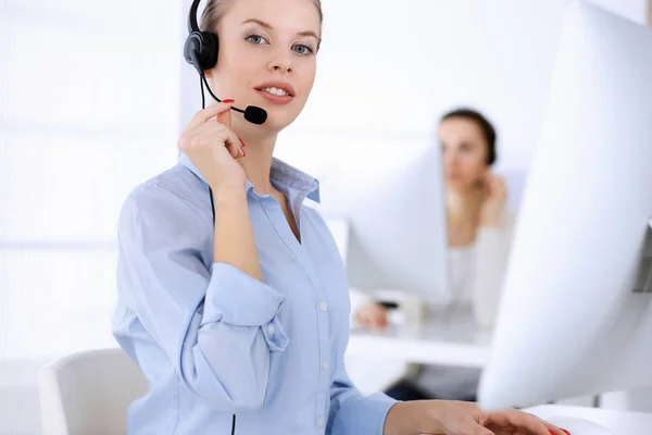 Call center office. Beautiful blonde woman using computer and headset for consulting clients online. Group of operators working as customer service occupation. Business people concept Stock Image