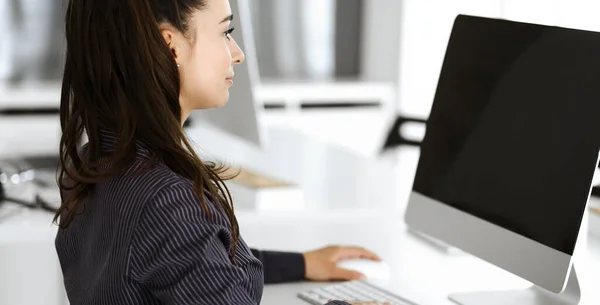 Бізнес-жінка використовує комп'ютер на робочому місці в сучасному офісі. Секретарка Брюнета або жінка-адвокат посміхається і виглядає щасливою. Праця за розвагами і успіхом — стокове фото