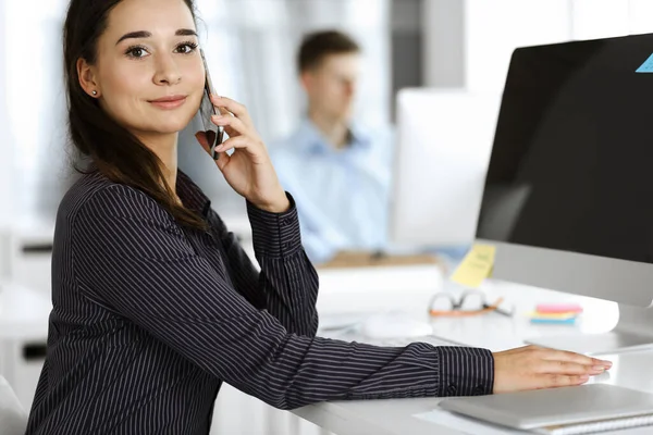 Business woman using computer at workplace in modern office. Brunette secretary or female lawyer smiling and looks happy. Working for pleasure and success