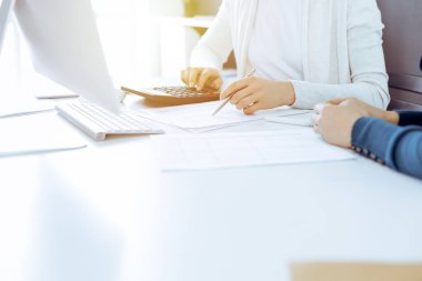 Muhasebeci mali durumu kontrol ediyor ya da vergi formları için hesap makinesi geliri ile sayıyor, eller yakın çekim. İş kadını ofisteki masada iş arkadaşıyla oturuyor ve çalışıyor. Denetim kavramı