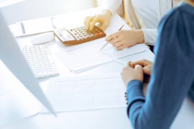 Muhasebeci mali durumu kontrol ediyor ya da vergi formları için hesap makinesi geliri ile sayıyor, eller yakın çekim. İş kadını ofisteki masada iş arkadaşıyla oturuyor ve çalışıyor. Denetim kavramı