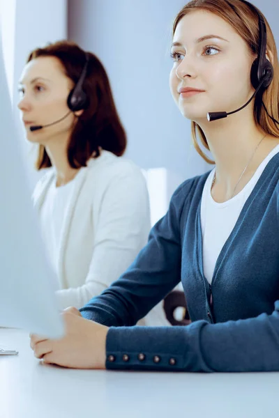 Call center. Group of operators at work. Focus on beautiful woman receptionist in headset at customer service office. Business concept