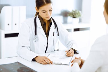 Kadın doktor ve hasta hastane ofisinde oturuyor ve konuşuyor. Yeşil renkli bluz terapiste uygun.