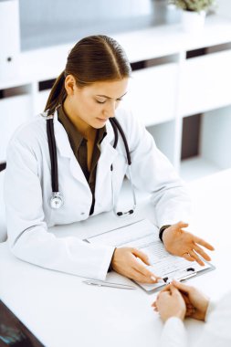 Kadın doktor ve hasta hastane ofisinde oturuyor ve konuşuyor. Yeşil renkli bluz terapiste uygun.