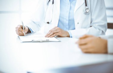 Bilinmeyen kadın-doktor ve kadın hasta klinikteki tıbbi muayenede oturuyor ve konuşuyor, yakın plan. Mavi bluz giyen terapist ilaç geçmişini dolduruyor. Tıp konsepti
