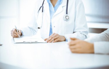 Bilinmeyen kadın-doktor ve kadın hasta klinikteki tıbbi muayenede oturuyor ve konuşuyor, yakın plan. Mavi bluz giyen terapist ilaç geçmişini dolduruyor. Tıp konsepti