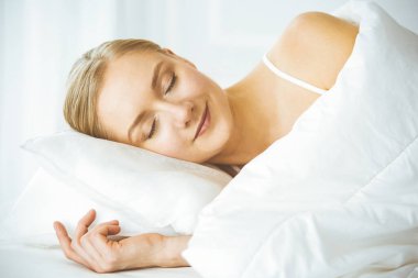 Güzel genç bir kadın yatak odasında rahat ve mutlu bir şekilde uyuyor. Mutlu bir sabah uyanıyorum.