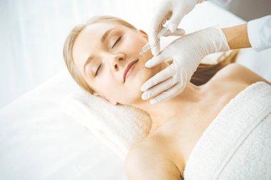 Güzellik doktoru sarışın kadın yüzüne şırıngayla güzellik prosedürü uyguluyor. Kozmetik tıp, güzellik enjeksiyonu konsepti