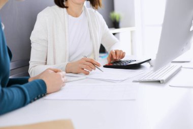 Mali durumu kontrol eden ya da vergi formları için hesap makinesinin geliri ile sayan, elleri yakın çekim. İş kadını, iş yerinde iş arkadaşıyla birlikte mavi tonda oturuyor. Vergi ve