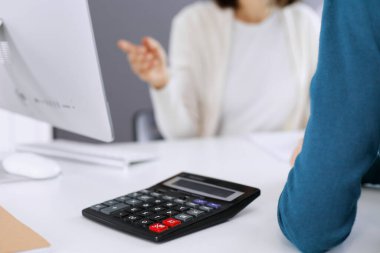 Mali durumu kontrol eden ya da vergi formları için hesap makinesinin geliri ile sayan, elleri yakın çekim. İş kadını, iş yerinde iş arkadaşıyla birlikte mavi tonda oturuyor. Vergi ve