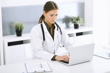 Hastane ofisindeki masada otururken dizüstü bilgisayarda yazan bir kadın doktor. Hekim iş başında. Tıp ve sağlık alanlarındaki veriler