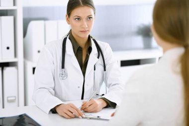 Kadın doktor ve hasta hastane ofisinde oturuyor ve konuşuyor. Yeşil renkli bluz terapiste yakışır. Tıp ve sağlık hizmetleri kavramı