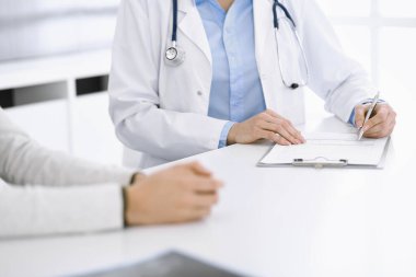 Bilinmeyen kadın-doktor ve kadın hasta klinikteki tıbbi muayenede oturuyor ve konuşuyor, yakın plan. Mavi bluz giyen terapist ilaç geçmişini dolduruyor. Tıp konsepti