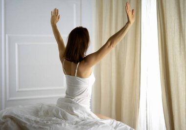 Bir kadın uyandıktan sonra yatakta geriniyor, geriye bakıyor, bir güne mutlu ve rahat giriyor iyi bir gece uykusundan sonra. Esmer için günaydın ve yeni bir gün. Hafta sonu kavramı, tatiller