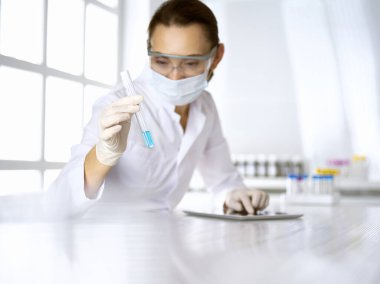 Kadın laboratuvar asistanı mavi sıvıyla test tüpünü analiz ediyor. Tıp, sağlık ve araştırma konsepti