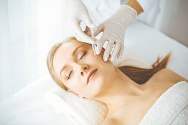 Güzellik doktoru sarışın kadın yüzüne şırıngayla güzellik prosedürü uyguluyor. Kozmetik tıp, güzellik enjeksiyonu konsepti