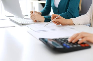 Muhasebeci mali durumu kontrol ediyor ya da vergi formları için hesap makinesi geliri ile sayıyor, eller yakın çekim. İş kadını ofisteki masada iş arkadaşıyla oturuyor ve çalışıyor. Denetim kavramı