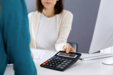 Muhasebeci mali durumu kontrol ediyor ya da vergi formları için hesap makinesi geliri ile sayıyor, eller yakın çekim. İş kadını ofisteki masada iş arkadaşıyla oturuyor ve çalışıyor. Denetim kavramı