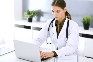 Hastane ofisindeki masada otururken dizüstü bilgisayarda yazan bir doktor. Hekim kadın iş başında. Tıp ve sağlık alanlarındaki veriler