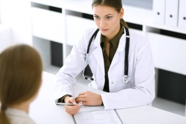 Kadın doktor ve hasta hastane muayenehanesinde oturup konuşuyorlar. Yeşil renkli bluz terapiste yakışır. Tıp ve sağlık hizmetleri kavramı