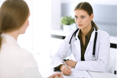 Kadın doktor ve hasta hastane muayenehanesinde oturup konuşuyorlar. Yeşil renkli bluz terapiste yakışır. Tıp ve sağlık hizmetleri kavramı