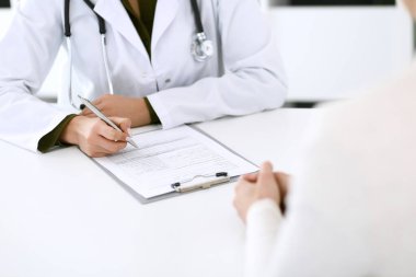 Kadın doktor ve hasta hastane muayenehanesinde oturuyor ve konuşuyor, yakın plan. İlaç kayıtlarını dolduran bir terapist. Tıp ve sağlık hizmetleri kavramı