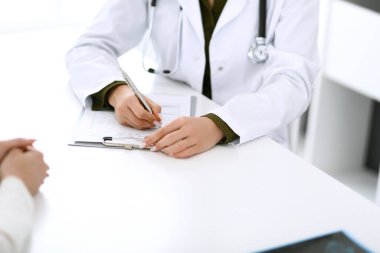 Kadın doktor ve hasta hastane muayenehanesinde oturuyor ve konuşuyor, yakın plan. İlaç kayıtlarını dolduran bir terapist. Tıp ve sağlık hizmetleri kavramı