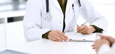 Kadın doktor ve hasta hastane muayenehanesinde oturuyor ve konuşuyor, yakın plan. İlaç kayıtlarını dolduran bir terapist. Tıp ve sağlık hizmetleri kavramı