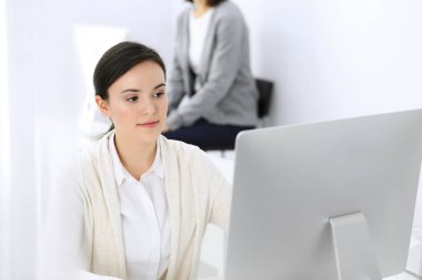 Ofiste bilgisayarla çalışan bir iş kadını, arka planda çalışan bir iş arkadaşı. Masada otururken avukatın ya da muhasebecinin vesikalığı.