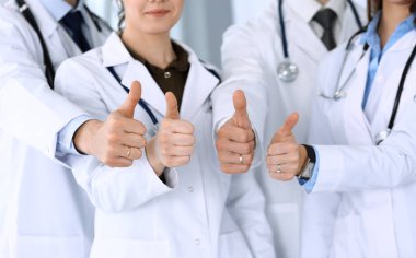Group of modern doctors standing as a team with thumbs up in hospital office. Physicians ready to examine and help patients. Medical help, insurance in health care, best desease treatment and medicine clipart