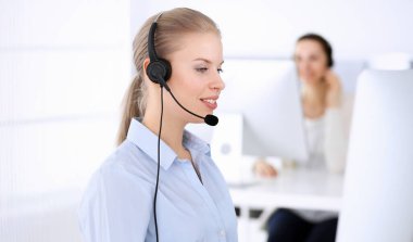 Merkezi ara. İnternette müşterilere danışmak için bilgisayar ve kulaklık kullanan güzel sarışın kadın. Müşteri hizmetleri işgali olarak çalışan bir grup operatör. İş adamları konsepti