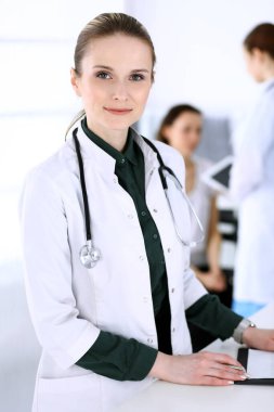 Doktor kadın hasta ve meslektaşı ile birlikte çalışıyor. Hastane resepsiyonunda dururken doktor tıbbi belge ya da reçete dolduruyor. Tıp ve sağlık hizmetlerindeki veriler