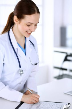 İşyerindeki doktor kadın. Hastane resepsiyonunda dururken tıp belgelerini dolduran doktor ya da dahili öğrenci. Tıp ve sağlık hizmetleri kavramındaki veriler