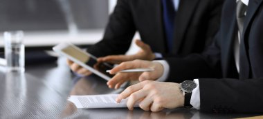 İşadamı tablet bilgisayar kullanıyor ve iş arkadaşı ya da ortağıyla modern ofiste cam masada çalışıyor. Yakın plan. Toplantıda bilinmeyen iş adamları var. Takım çalışması ve ortaklık kavramı