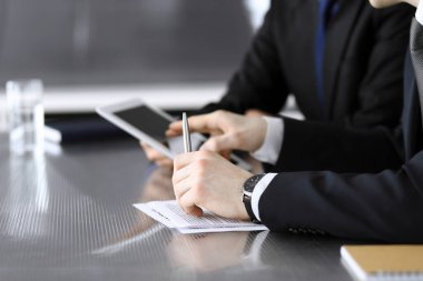 İşadamı tablet bilgisayar kullanıyor ve iş arkadaşı ya da ortağıyla modern ofiste cam masada çalışıyor. Yakın plan. Toplantıda bilinmeyen iş adamları var. Takım çalışması ve ortaklık kavramı