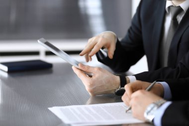 İşadamı tablet bilgisayar kullanıyor ve iş arkadaşı ya da ortağıyla modern ofiste cam masada çalışıyor. Yakın plan. Toplantıda bilinmeyen iş adamları var. Takım çalışması ve ortaklık kavramı