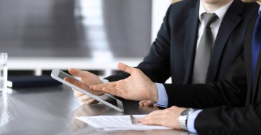 İşadamı tablet bilgisayar kullanıyor ve iş arkadaşı ya da ortağıyla modern ofiste cam masada çalışıyor. Yakın plan. Toplantıda bilinmeyen iş adamları var. Takım çalışması ve ortaklık kavramı