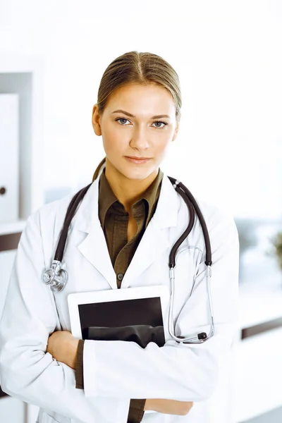 Женщина-врач стоит и смотрит в камеру. Идеальное медицинское обслуживание в клинике — стоковое фото