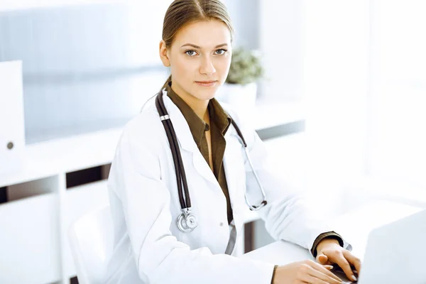 Kvinna-läkare skriva på bärbar dator medan du sitter vid skrivbordet på sjukhuset kontor. Läkare på jobbet — Stockfoto