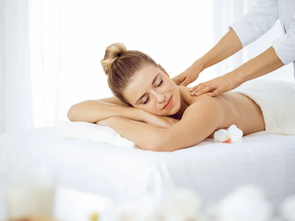 Young and blonde woman enjoying massage of back in spa salon. Beauty concept — Stock Photo, Image