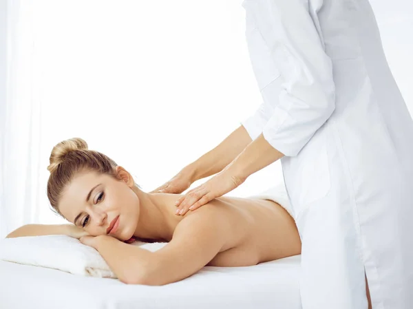 Young and blonde woman enjoying massage of back in spa salon. Beauty concept — Stock Photo, Image