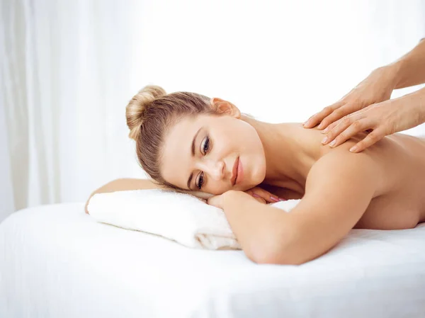 Young and blonde woman enjoying massage of back in spa salon. Beauty concept — Stock Photo, Image