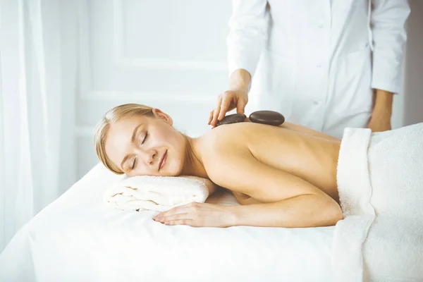 Beautiful happy woman enjoying warm stones procedure with closed eyes. Beauty and Spa salon concept — Stock Photo, Image