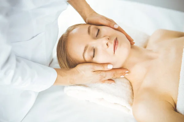 Hermosa mujer feliz disfrutando de masaje facial con los ojos cerrados en el salón de spa. Tratamiento relajante en medicina y concepto de belleza — Foto de Stock