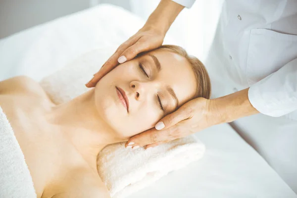 Hermosa mujer feliz disfrutando de masaje facial con los ojos cerrados en el salón de spa. Tratamiento relajante en medicina y concepto de belleza — Foto de Stock