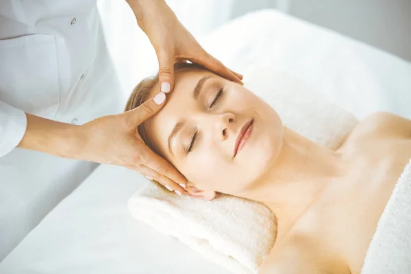 Красива щаслива жінка насолоджується масажем обличчя з закритими очима в спа-салоні. Розслаблююче лікування в медицині та концепції краси — стокове фото