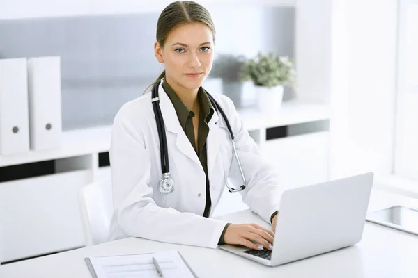 Žena-doktor psaní na notebooku, zatímco sedí za stolem v nemocniční kanceláři. Lékař v práci. Údaje v medicíně a zdravotnictví — Stock fotografie