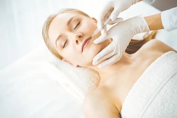 Beautician doctor doing beauty procedure with syringe to blonde female face. Cosmetic medicine, beauty injections concept