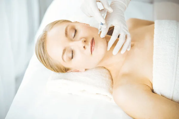 Beautician doctor doing beauty procedure with syringe to blonde female face. Cosmetic medicine, beauty injections concept