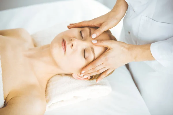Hermosa mujer feliz disfrutando de masaje facial con los ojos cerrados en el salón de spa. Tratamiento relajante en medicina y concepto de belleza — Foto de Stock
